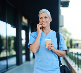 Nurse in scrubs enjoying coffee and using a mobile phone outside a modern medical facility during a...
