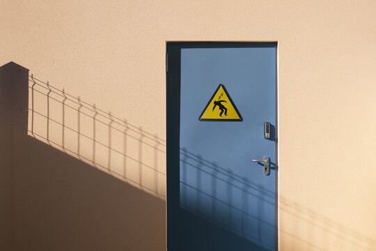 Porte en m&eacute;tal bleue s&eacute;curis&eacute;e par un digicode d'un local technique &eacute;lectrique avec panneau danger &eacute;lectrocution fix&eacute; dessus.