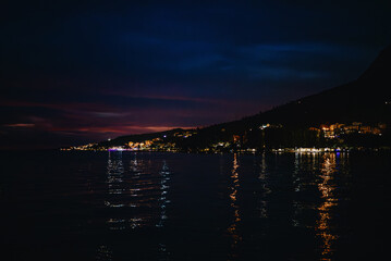Night coastline with city lights and dark sea reflection. © M-Production