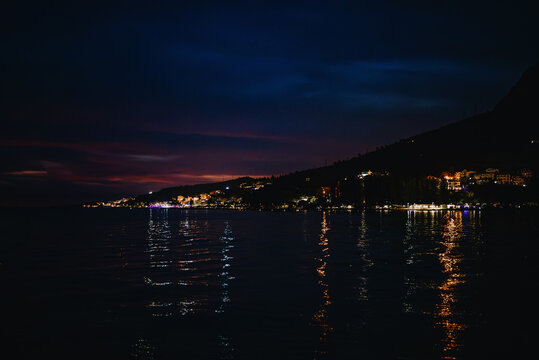 Night coastline with city lights and dark sea reflection.