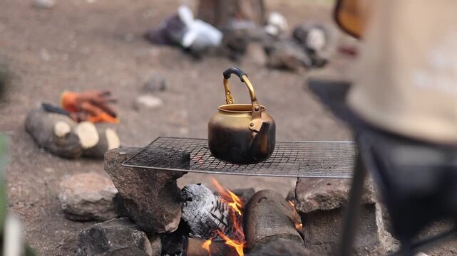 Traditional Kettle Boiling Water on Campfire in Nature &ndash; Outdoor Camping Life
A cinematic 4K video showing a vintage golden kettle placed on a grill over a real wood fire. Steam rises as the water boi