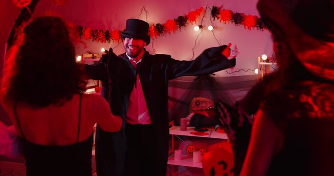 Happy Halloween friends gather, holiday people dancing wearing costumes for dress ups party night event, playing spooky horror cosplay look, garland red light decor atmosphere, lantern decor at home