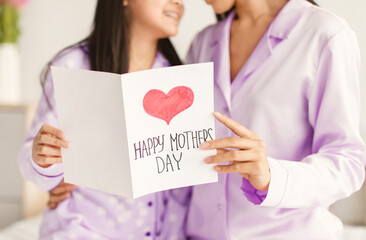Two people are sharing a special moment on Mother's Day while reading a card. They are wearing matching purple pajamas. A heart is drawn on the card. © Prostock-studio