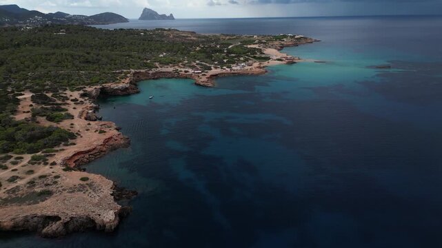 Aerial view of Cala Comte Bay in Ibiza, taken by drone, highlighting the turquoise reflections on the water; in the background, you can see the island of Es Vedra. Spain, Balearic Islands.