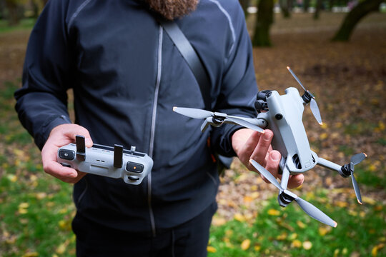 Man holds drone and controller, preparing for flight. Bearded man checking quadcopter and remote control in a park, getting ready for aerial photography, concept of modern technology and hobby