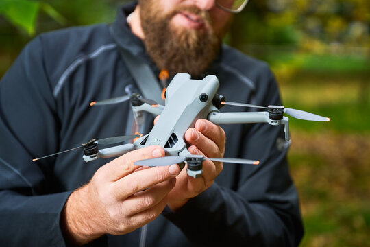 Man holds drone and checks its condition before flight. Close up of hands examining quadcopter in park, inspecting body and propellers, concept of modern technology and maintenance
