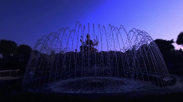 Silhouette of Goddess Durga statue behind water fountain at sunset in India. Dramatic spiritual scene with flowing water, golden sky, and temple ambiance, Chaar Dham Temple in Vrindavan, Uttar Pradesh