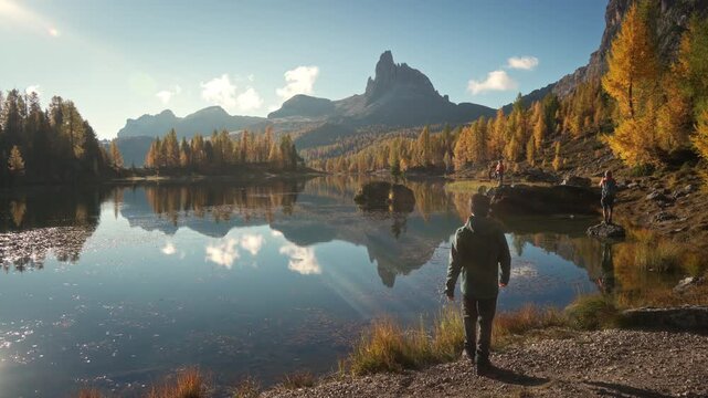 Scenic autumn landscape of male hiker visiting at Lago di Federa with Croda da Lago peak surrounded by larch forest in Dolomites, Italy