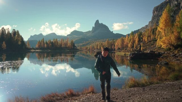 Scenic autumn landscape of male hiker visiting at Lago di Federa with Croda da Lago peak surrounded by larch forest in Dolomites, Italy