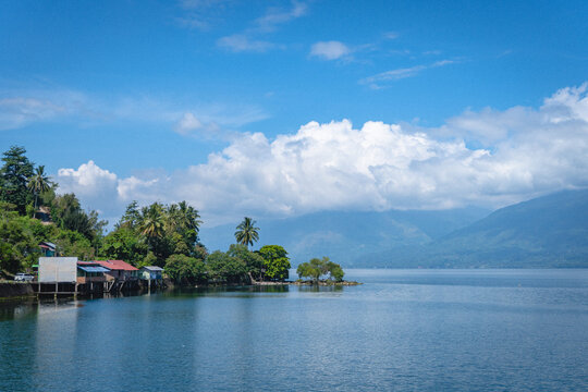 Lake Singkarak landscape in West Sumatra, Indonesia, featuring calm water, lakeside houses, and mountain backdrop under blue sky, showcasing serene nature and travel destination.