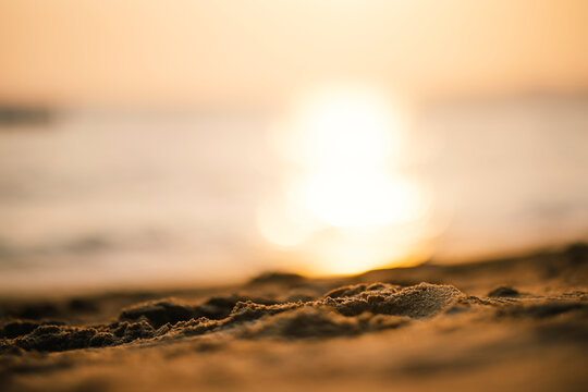 A beautiful blurred sunset reflects on the ocean with a close-up of golden sand in the foreground. Perfect for summer or peaceful concepts.