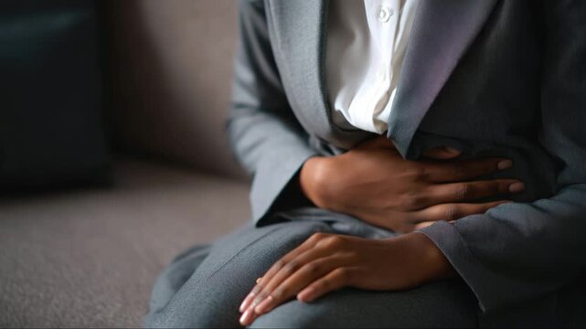 A young businesswoman experiences abdominal pain due to anxiety at work. The woman holds her stomach with her hands. Concepts: pain, anxiety, psychosomatics
