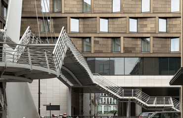 Unspooling like a metallic ribbon, the silver staircase of the Millennium Bridge cuts a dynamic path through the air, its airy, kinetic form standing in stark relief against a solid, bronze-hued facad