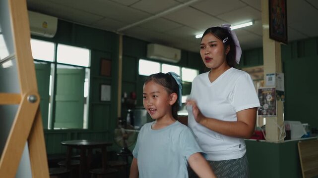 An Asian girl dances smiling as her mother combs her hair on a hot summer day