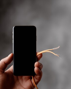 hand holding damaged smartphone charging cable with frayed wires, technology failure concept, electrical hazard and repair need
