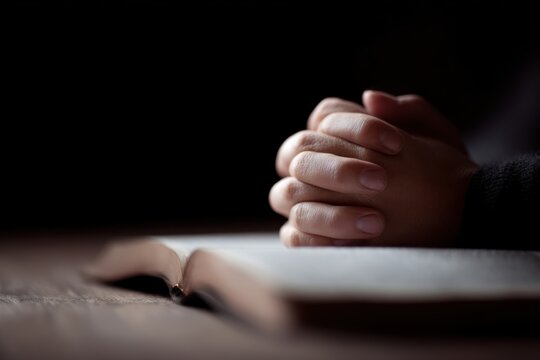 Hands clasped in prayer on open Bible spiritual devotion concept