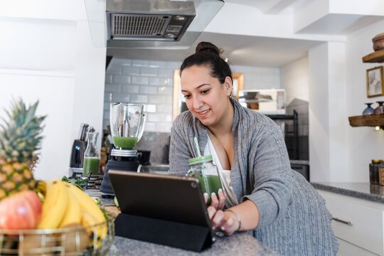 young latina woman overweight drinking detox or green juice in kitchen at home in Mexico Latin America, Hispanic female plus size preparing vegetables beverage for diet