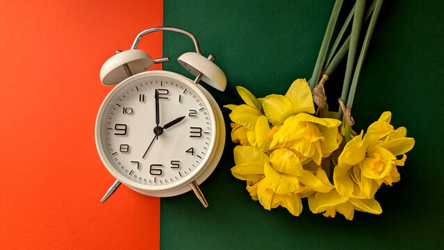 Daylight saving time concept &ndash; vintage alarm clock showing 2 AM with blooming narcissus on green and orange background. 