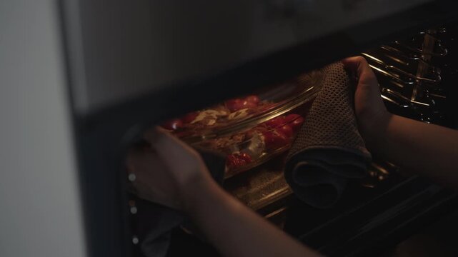 Chef female baking healthy homemade dish with feta cheese, cherry tomatoes and tuna in oven, removing glass casserole with oven mitt for delicious meal, close-up, slow motion.