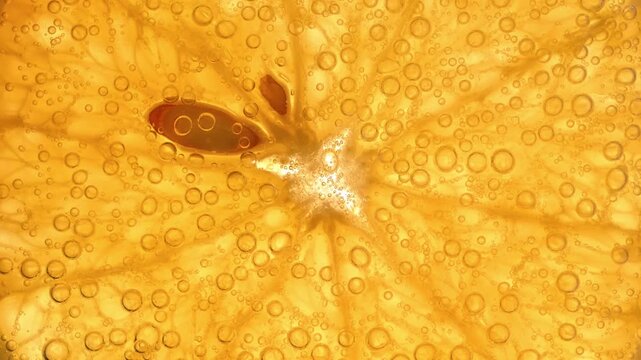 Macro shot of orange slice in sparkling water with rising and popping bubbles. Effervescent citrus texture creates refreshing abstract background with dynamic motion and vivid details