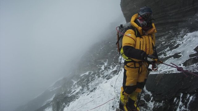 High altitude mountaineer rappelling down a steep, snowy rock face in the Himalayas