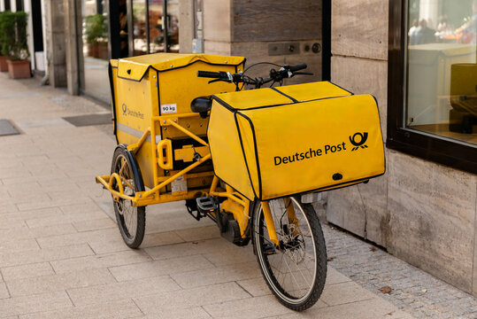HAMBURG, GERMANY - MARCH 7, 2026: A yellow Deutsche Post electric cargo bike parked on a city sidewalk for mail and parcel delivery in an urban environment