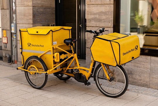 HAMBURG, GERMANY - MARCH 7, 2026: A side view of a yellow Deutsche Post electric cargo tricycle parked on a sidewalk for urban mail and parcel delivery
