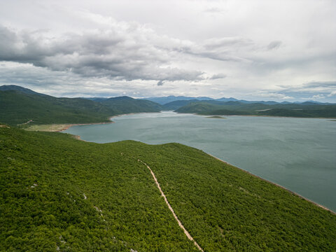 Bosnia and Herzegovina Vlahinja - 05 29 2025 Landscape drone photo of Bileća Lake, dense forest, rolling hills, and distant mountains in Vlahinja, Bosnia under a cloudy sky.
