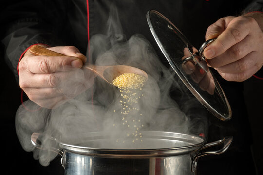 Hands pour grains Panicum into a pot while steam rises, showing a cooking scene in a kitchen