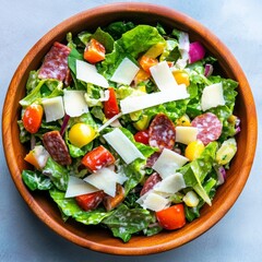 Vibrant overhead shot of a fresh, hearty salad in a wooden bowl, packed with crisp greens, savory salami, Parmesan and colorful cherry tomatoes., Italian, Meal