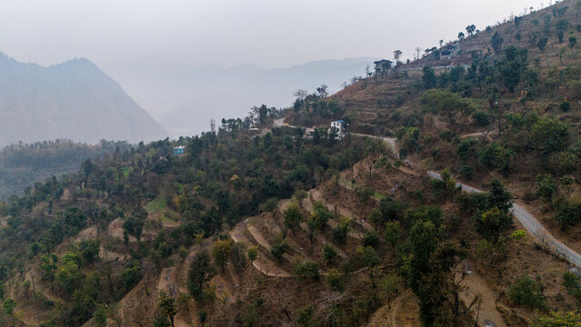 Aerial view of the landscape near Dwara village, Dehradun, Uttarakhand, showing misty mountains and forested hills under a calm winter evening sky.