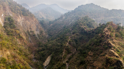 Obraz premium Aerial view of the Song River in Maldevta near Dehradun, Uttarakhand, showing low water flow in winter with a village house, greenery, and dirt roads across the mountain landscape.