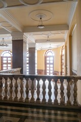 Fototapeta premium Large old European hall with intricate designs, tall arched windows, polished floors, columns, chandeliers, and an ornate balcony Warm color palette, natural light filtering in