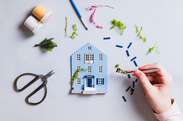 A child's hand decorates a house figurine with a plant, top view