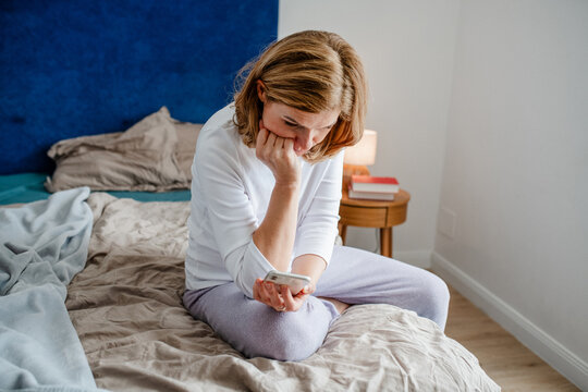 Mature woman using smartphone while sitting on bed.