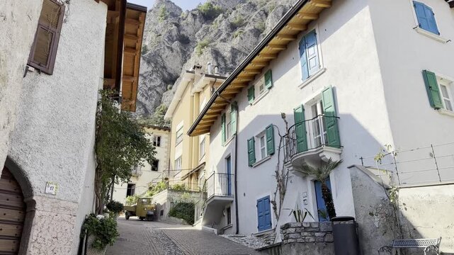 Charming Cobblestone Alley with Colorful Shutters Iron Benches Wooden Door and Rocky Mountain in Historic Old Town of Limone sul Garda Italy 4K HDR