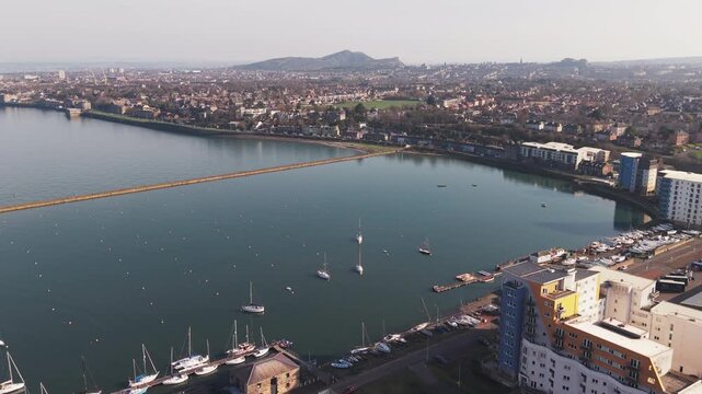 Wide aerial view of Granton district and long stone pier stretching into the sea towards Edinburgh city skyline, Scotland