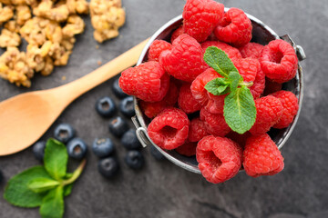 Fresh Raspberries with Mint in Metal Bucket with Blueberries, Granola and Wooden Spoon on Dark Slate — Healthy Berry Food Photography © Jan