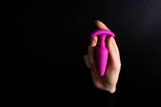Human hand holding pink silicone anal plug sex toy against dark background, studio lighting emphasizing smooth surface and ergonomic form.