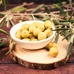 Bowl of green olives on wooden slice with olive branches