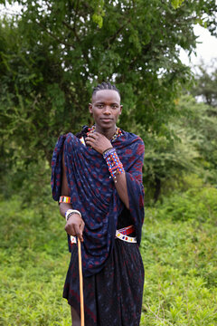 Portrait of a young Maasai warrior in the forest wearing traditional clothing and holding a wooden stick