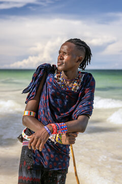 Young Maasai man in traditional attire wearing bead jewellery and holding a wooden stick