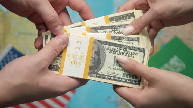 Businessmen exchange stack of dollars against US and Saudi flags with world map, indicating investments.