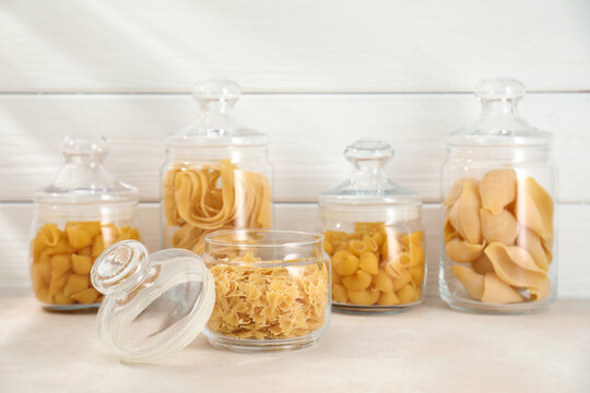 Different types of pasta in glass jars on beige table