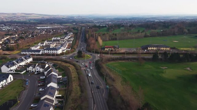 Road traffic on A7 with roundabout between Eskbank residential district and green parkland in Midlothian, Scotland