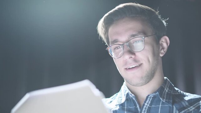 Confident young man standing on stage under dramatic spotlight holding script or notes. Speaker presenting, rehearsing or performing in theater, lecture or business presentation setting. Concept of