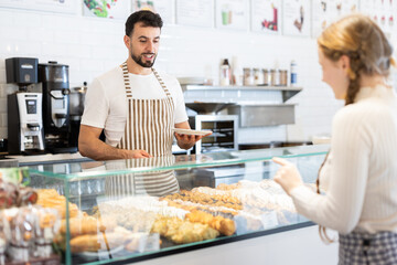 Guy canteen worker waits for customers near bakery counter, ready willing to sell fresh bun, help...