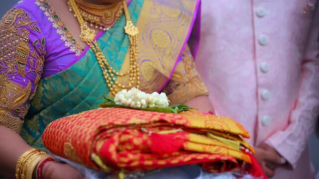 Women holding traditional offering plates with ceremonial items during Indian wedding ritual. Close-up shoot of cultural preparation in colorful ethnic attire.