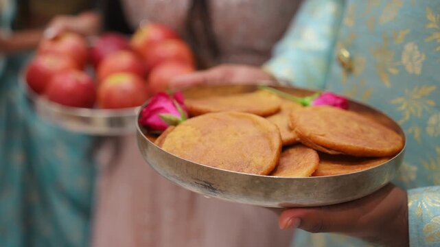 Women holding traditional offering plates with ceremonial items during Indian wedding ritual. Close-up shoot of cultural preparation in colorful ethnic attire.