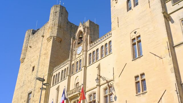 Narbonne medieval stone castle tower with clock and flags under clear blue sky
